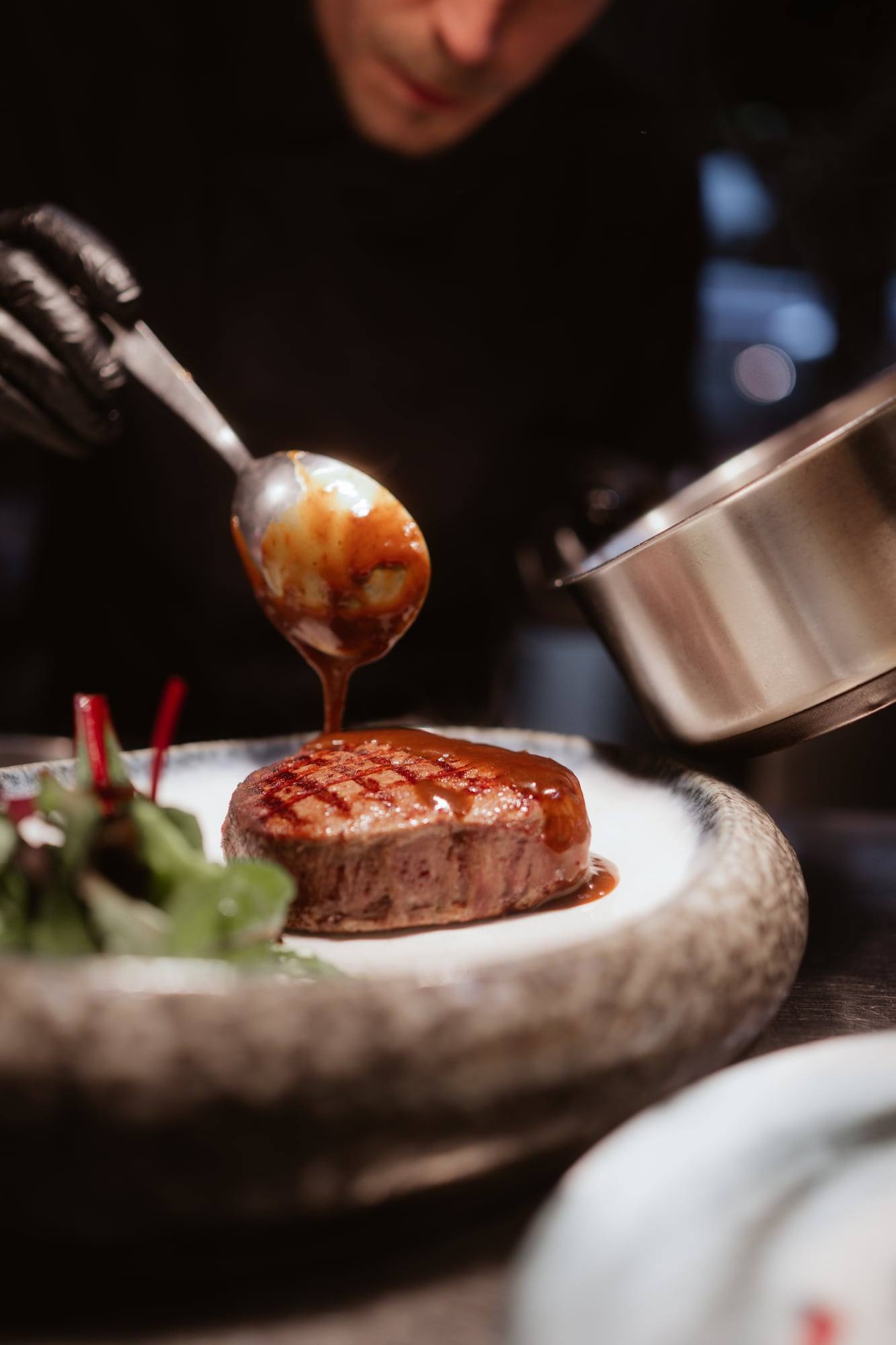 Koch gießt Sauce über ein Steak auf dem Teller