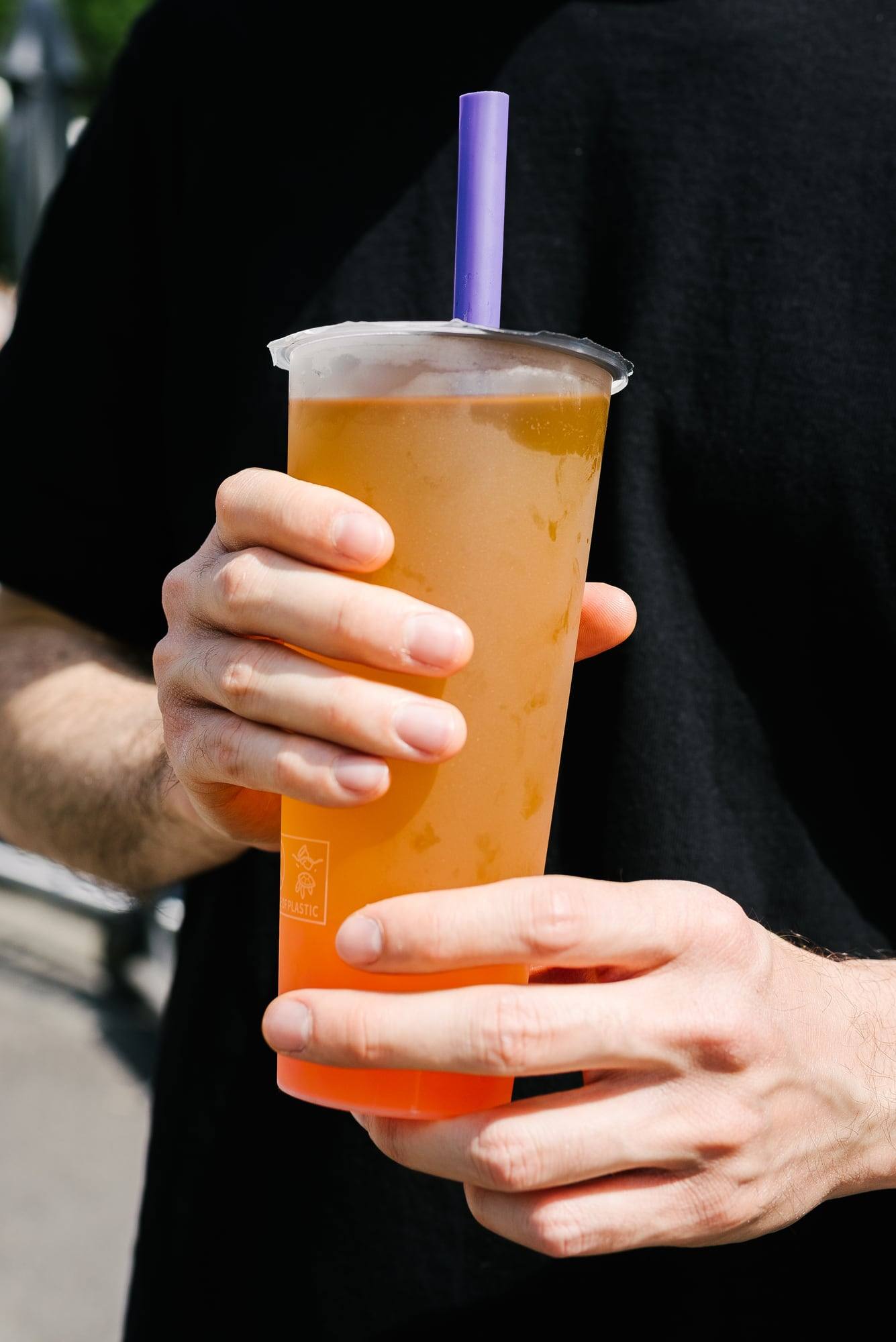 Hände halten einen orangen Bubble Tea mit Strohhalm