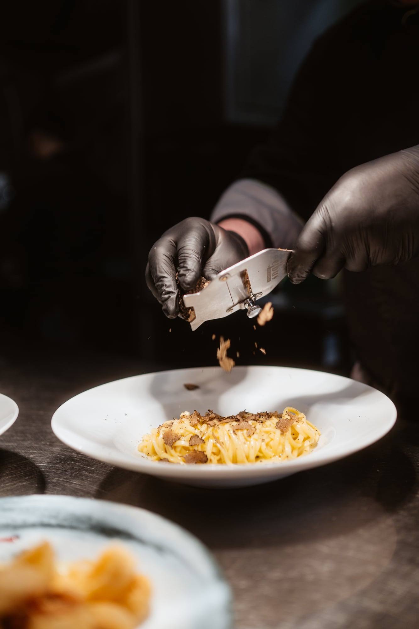 Koch richtet Pasta mit der Zange auf dem Teller an