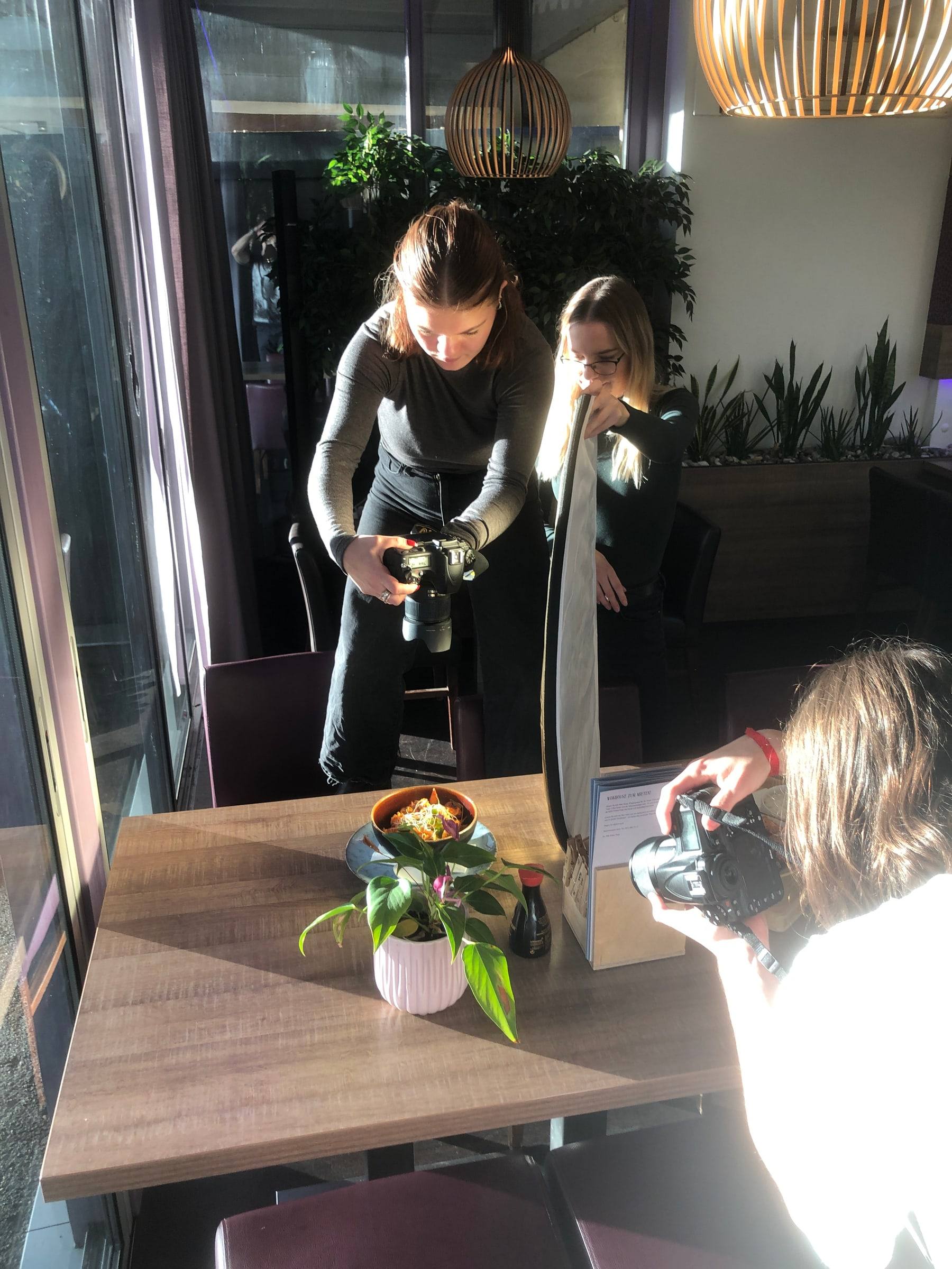 Fotografin mit Kamera, daneben eine Kollegin mit Reflektor beim Food-Shooting