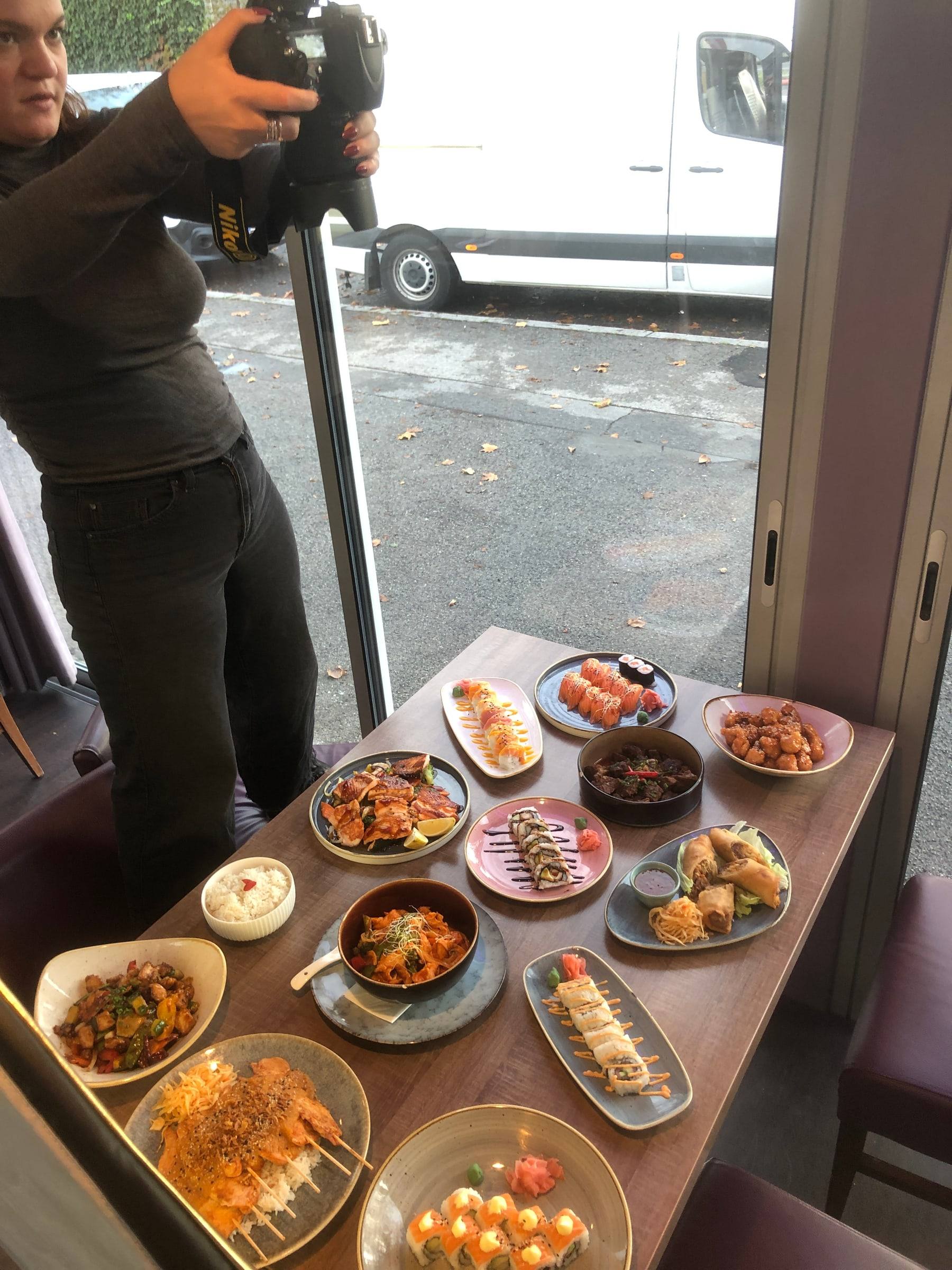 Fotografin fotografiert einen voll gedeckten Tisch mit Sushi und Wok-Gerichten von oben